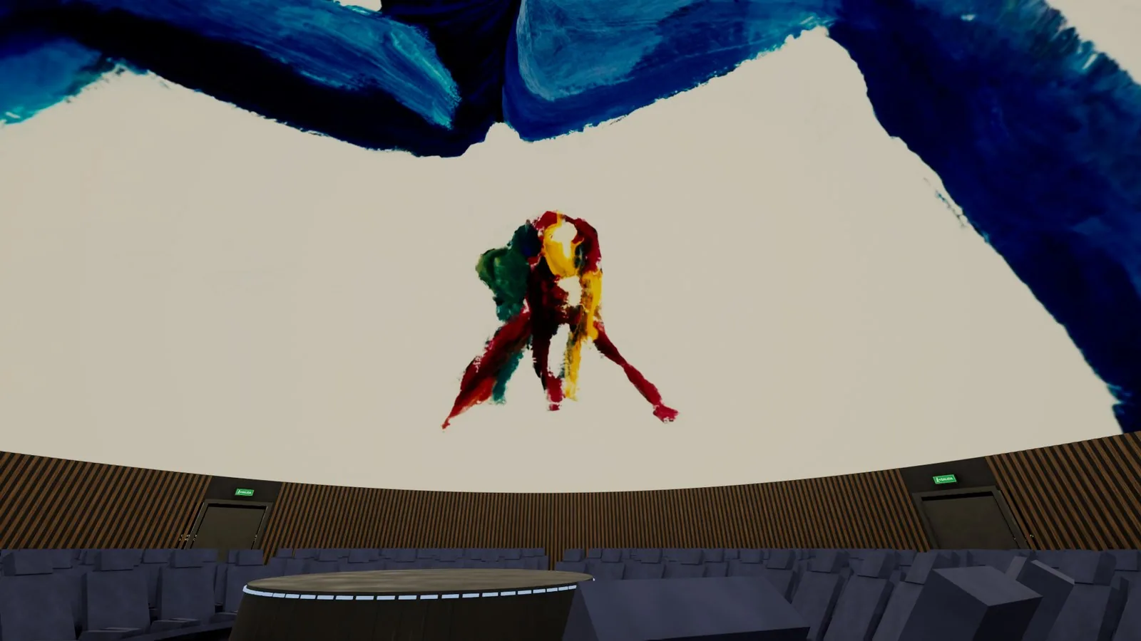 Una figura pintada en rojo, amarillo y verde flota en lo alto de una cúpula clara, sobre las butacas de un planetario.