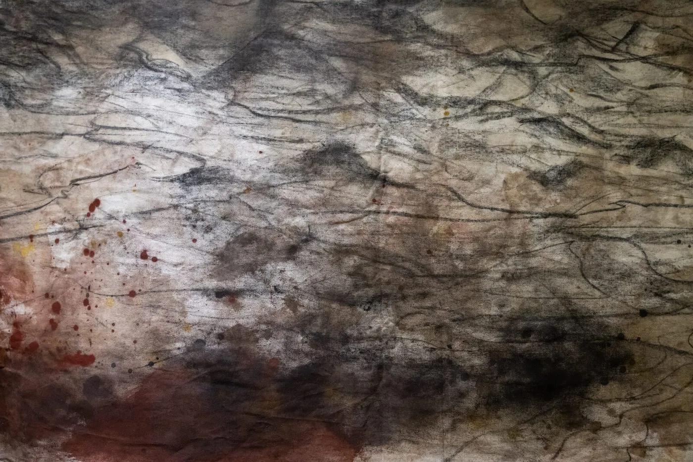Dettaglio del telo tinto: fumo nero e ocra sbavati sul cotone, linee di carbone come creste di montagna e schizzi rossi e gialli nell'angolo sinistro.