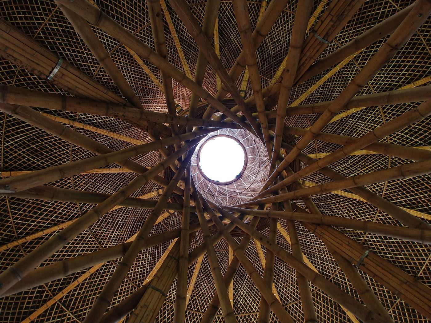 Techo de guadua visto desde el suelo: las cañas giran en espiral hacia un óculo circular por el que entra la luz.