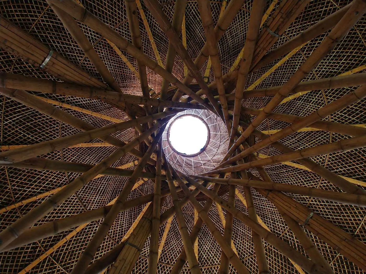 Tetto di guadua visto da terra: le canne girano a spirale verso un oculo circolare da cui entra la luce.