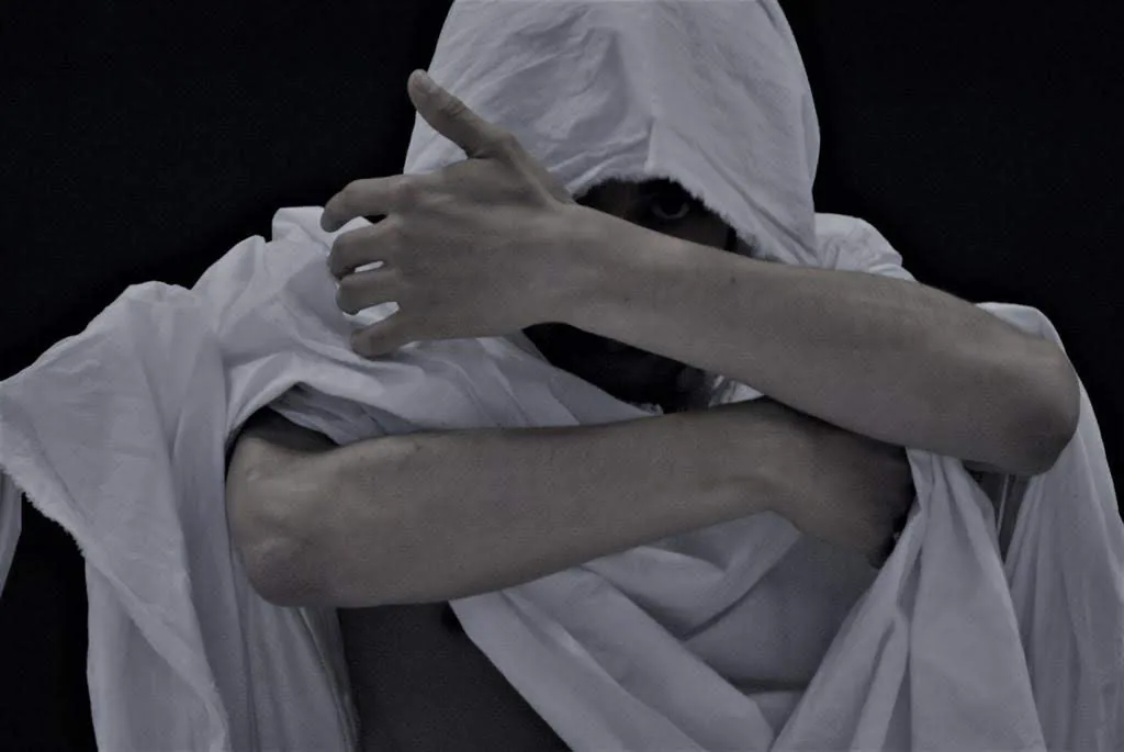Ballerino con un mantello bianco che si copre il volto con le braccia incrociate