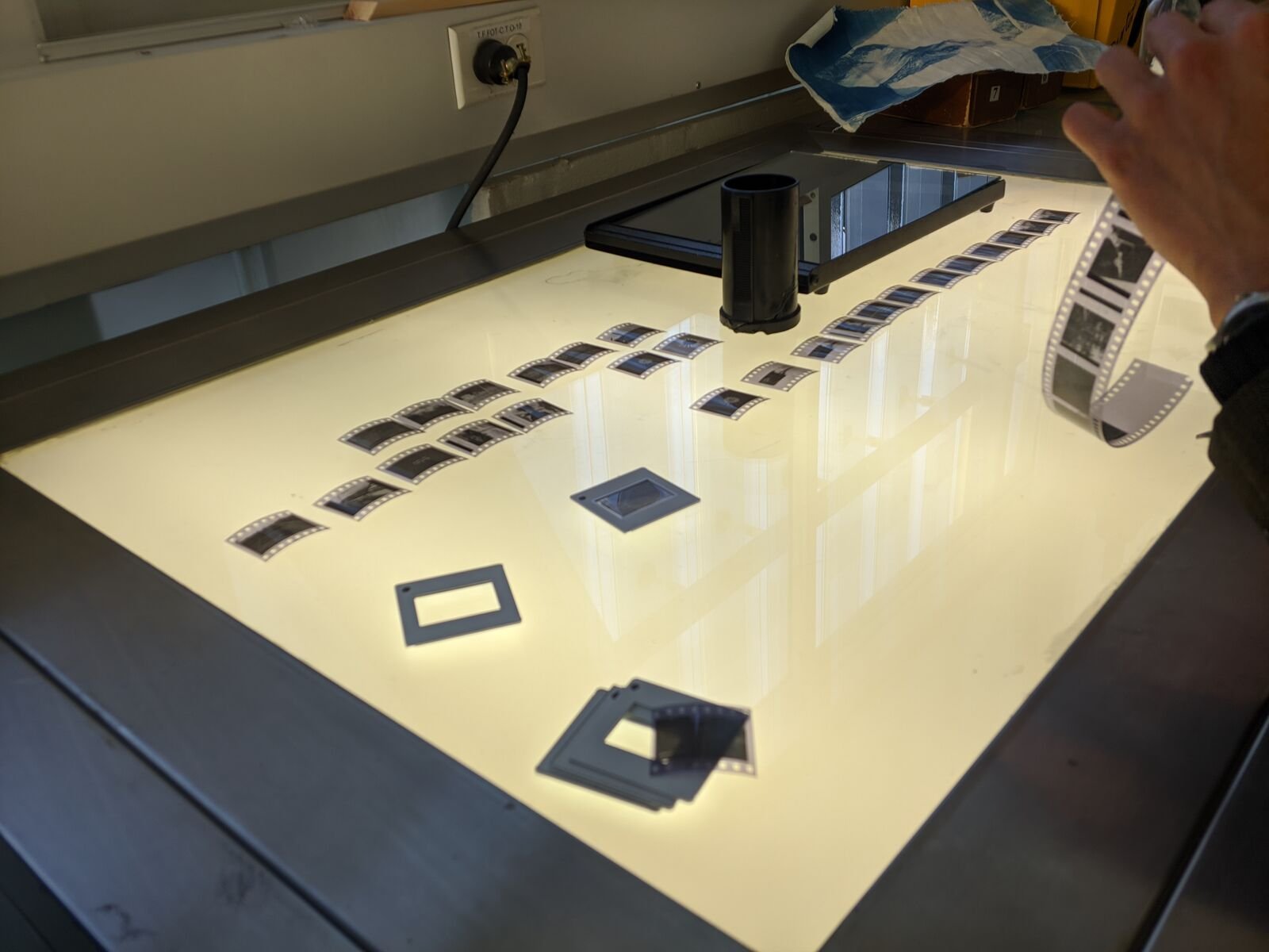 Mesa de luz con cuadros sueltos de película de 35 mm, una tira enrollada y marcos de diapositiva vacíos.
