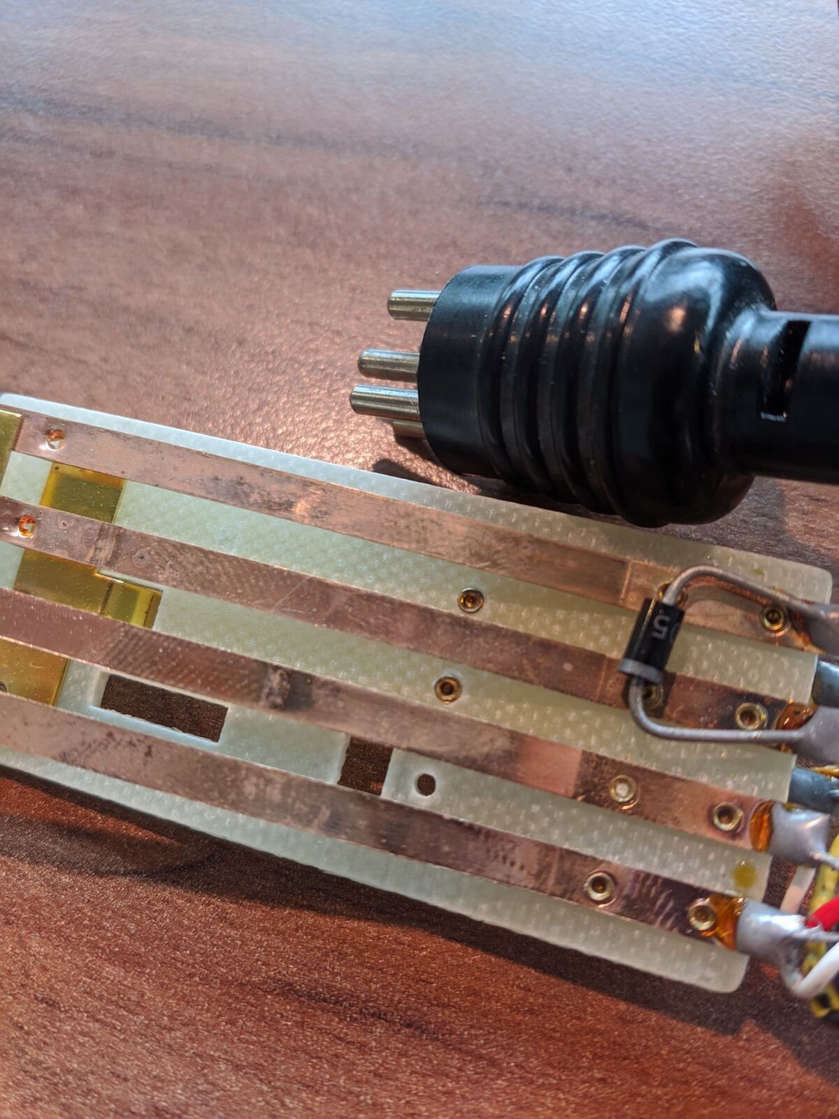 Placa de contactos de cobre del control remoto de un proyector junto al conector de pines del cable, sobre una mesa de madera.