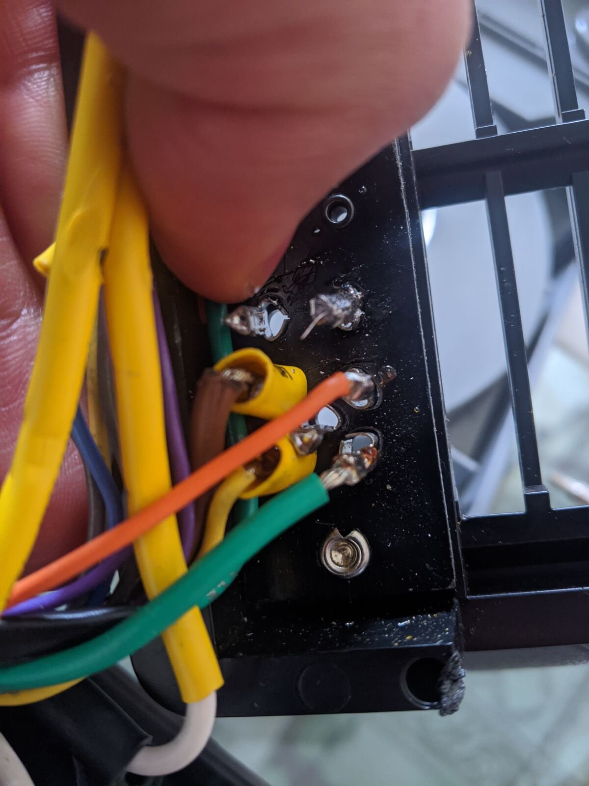 Mano que sostiene el conector trasero de un proyector con cables amarillo, café, naranja, verde y blanco soldados a los pines.